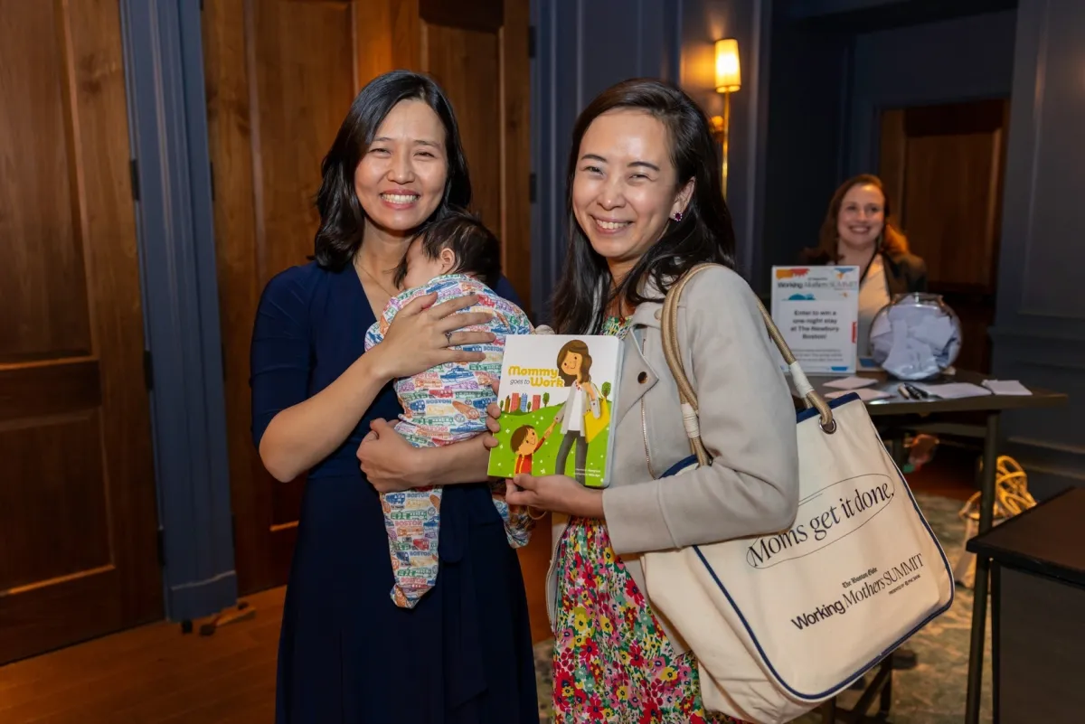 Mayor Michelle Wu holding her baby, standing beside Jossy Lee who is holding Mommy Goes to Work, at the inaugural Boston Globe Working Mothers Summit