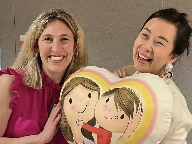 Jossy and a team member holding a heart-shaped Mommy Goes to Work pillow