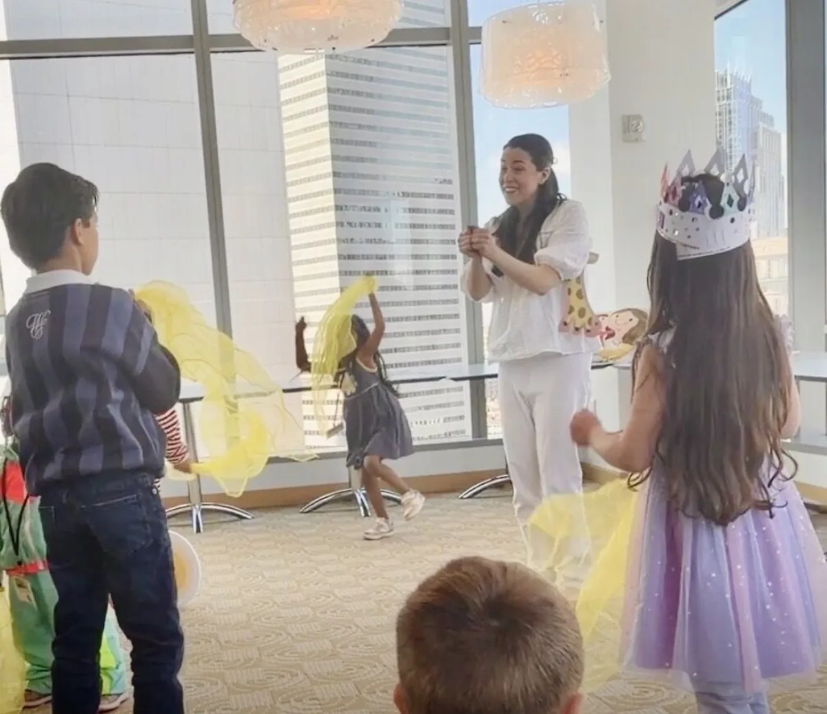 Children dancing with yellow scarves as an educator leads the Mommy Goes to Work song