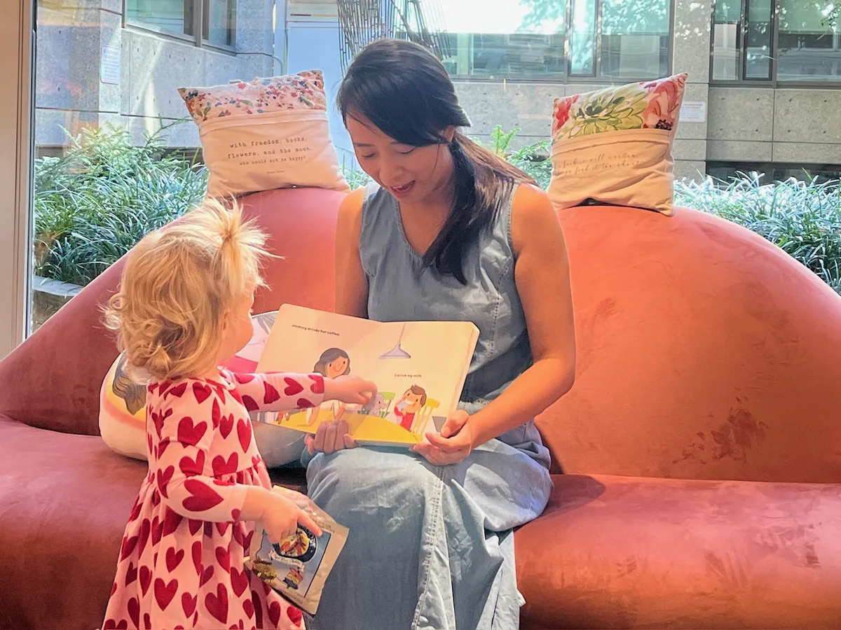 Jossy reading Mommy Goes to Work aloud to a toddler on a sofa