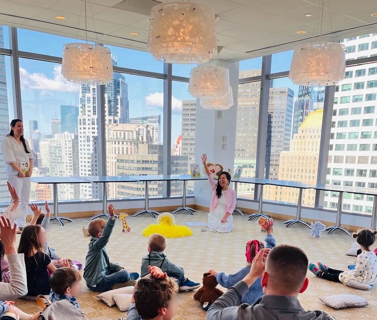 A room of little ones on cushions with their hands up at a Bring Your Child to Work Day story session