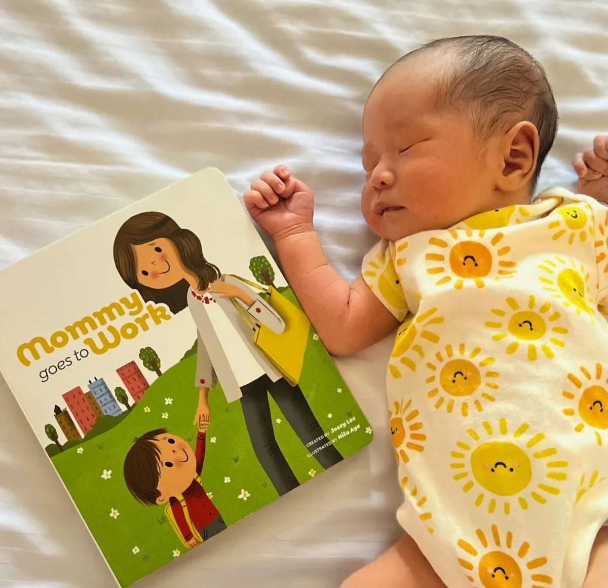 A newborn asleep beside a copy of Mommy Goes to Work