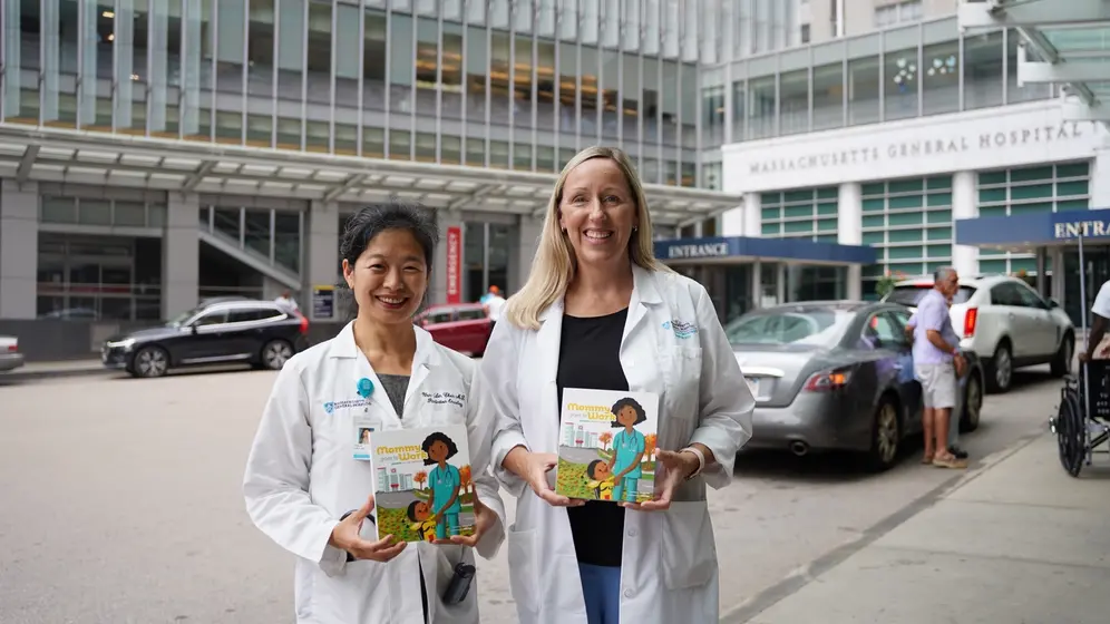 Two doctors in white coats holding the book outside Massachusetts General Hospital