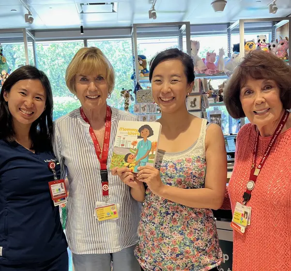 Four women from the hospital gift shop team holding the book