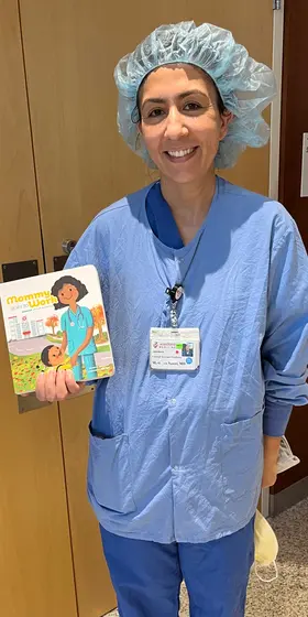 A nurse in scrubs and a surgical cap holding the book