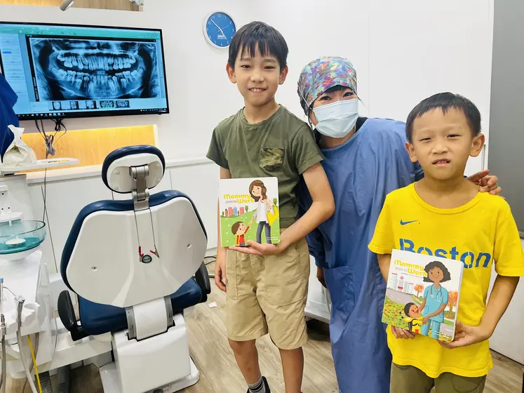A dentist with two boys holding the books in a dental office
