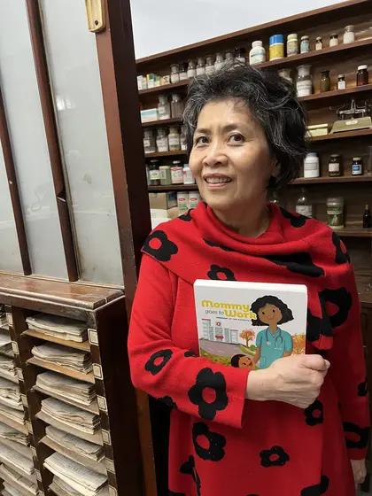 A pharmacist holding the book in front of a pharmacy cabinet