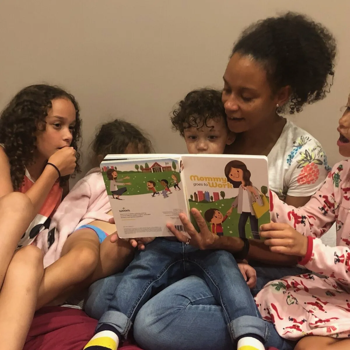 A mother reading the book to four children in pyjamas
