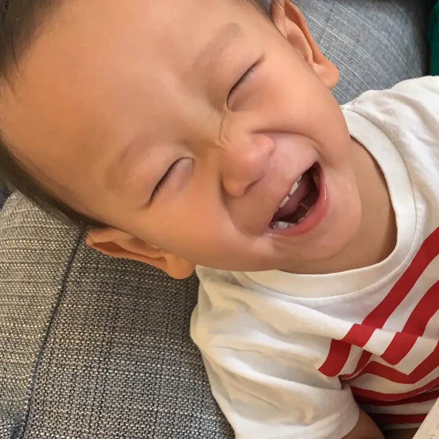 A baby laughing with their eyes screwed shut